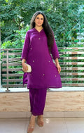 Woman in a purple outfit standing in front of a window with greenery outside